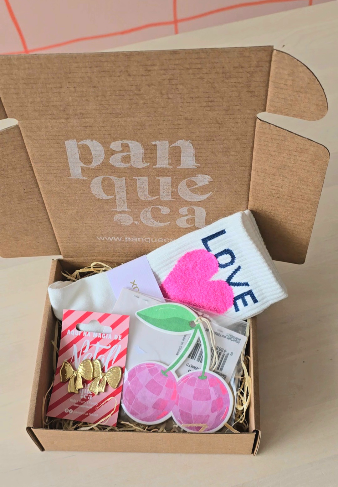 Caixa de cartão castanho aberta com vários acessórios e meias coloridas dentro