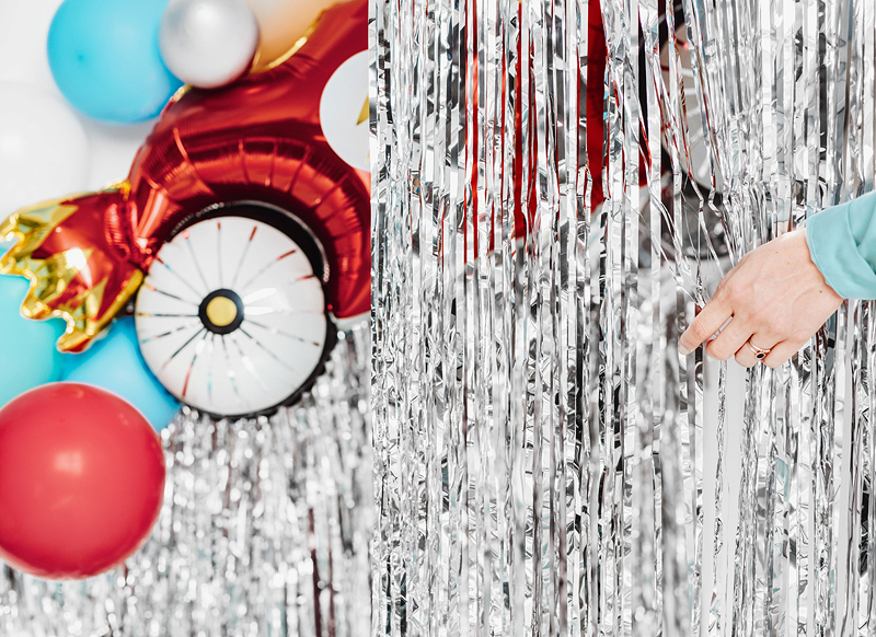 Cortina metálica prateada com balões coloridos e mão segurando fitas