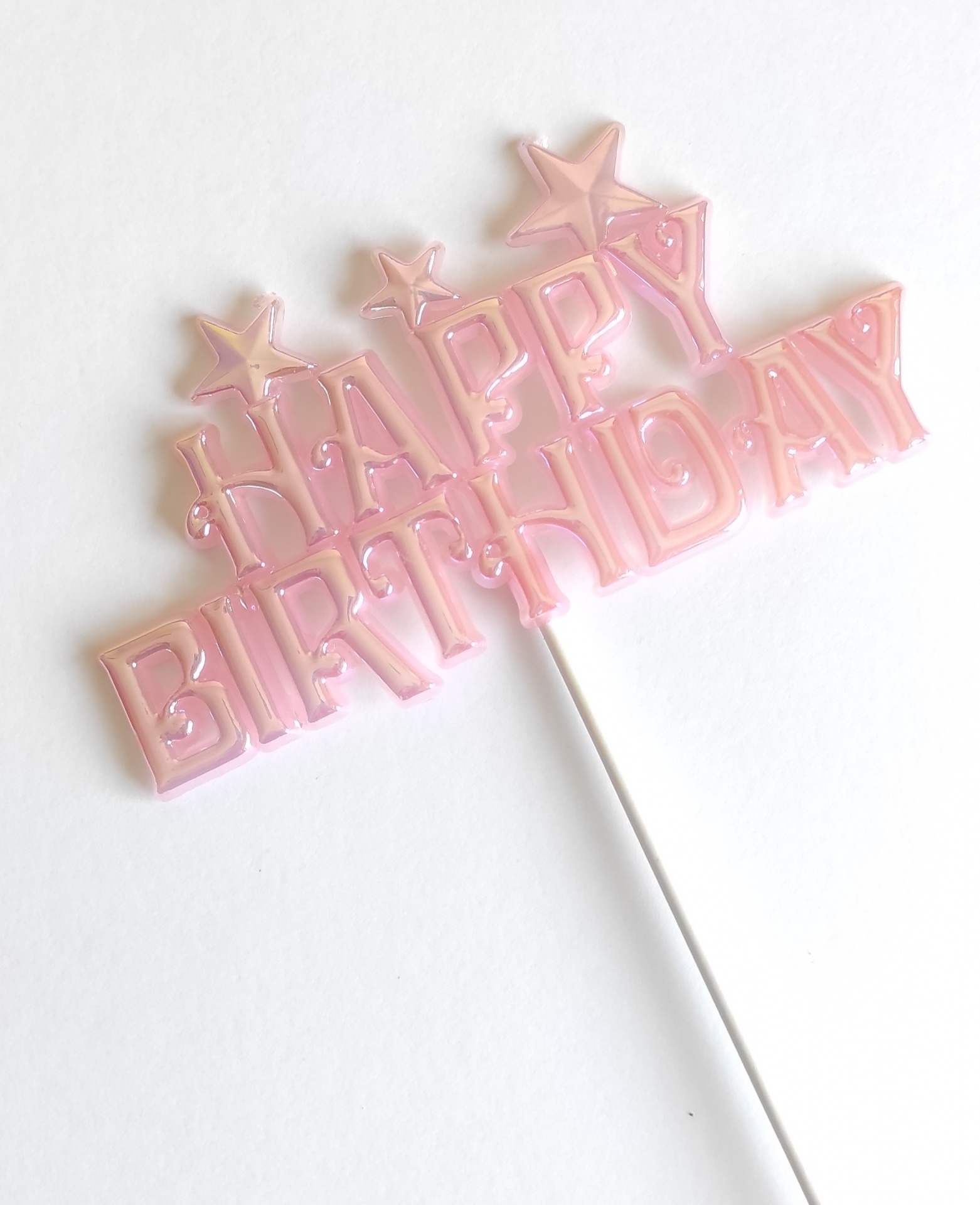 Topo de bolo cor-de-rosa translúcido com texto HAPPY BIRTHDAY em letras maiúsculas e estrelas