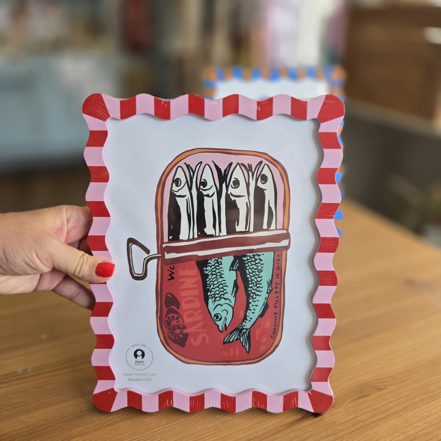Moldura decorativa com ilustração de lata de sardinhas e padrão vermelho e rosa em madeira