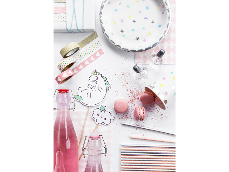 Mesa com artigos de festa em tons pastel, incluindo pratos com padrão de estrelas, macarrons cor-de-rosa e garrafas rosadas.