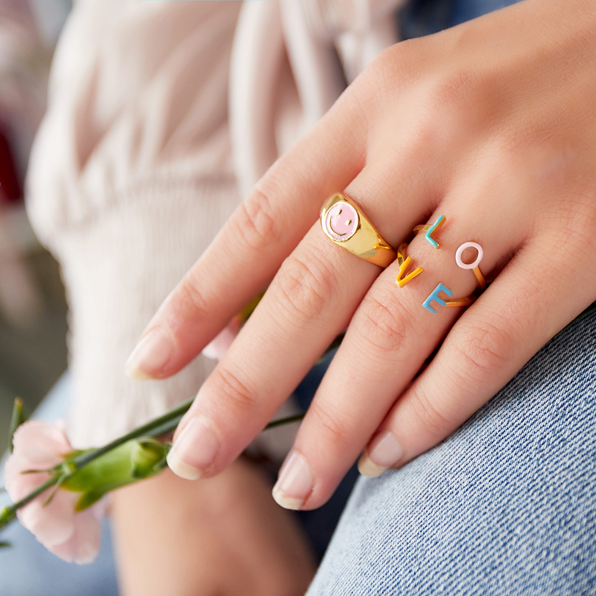 Mão com dois anéis coloridos e flor cor-de-rosa