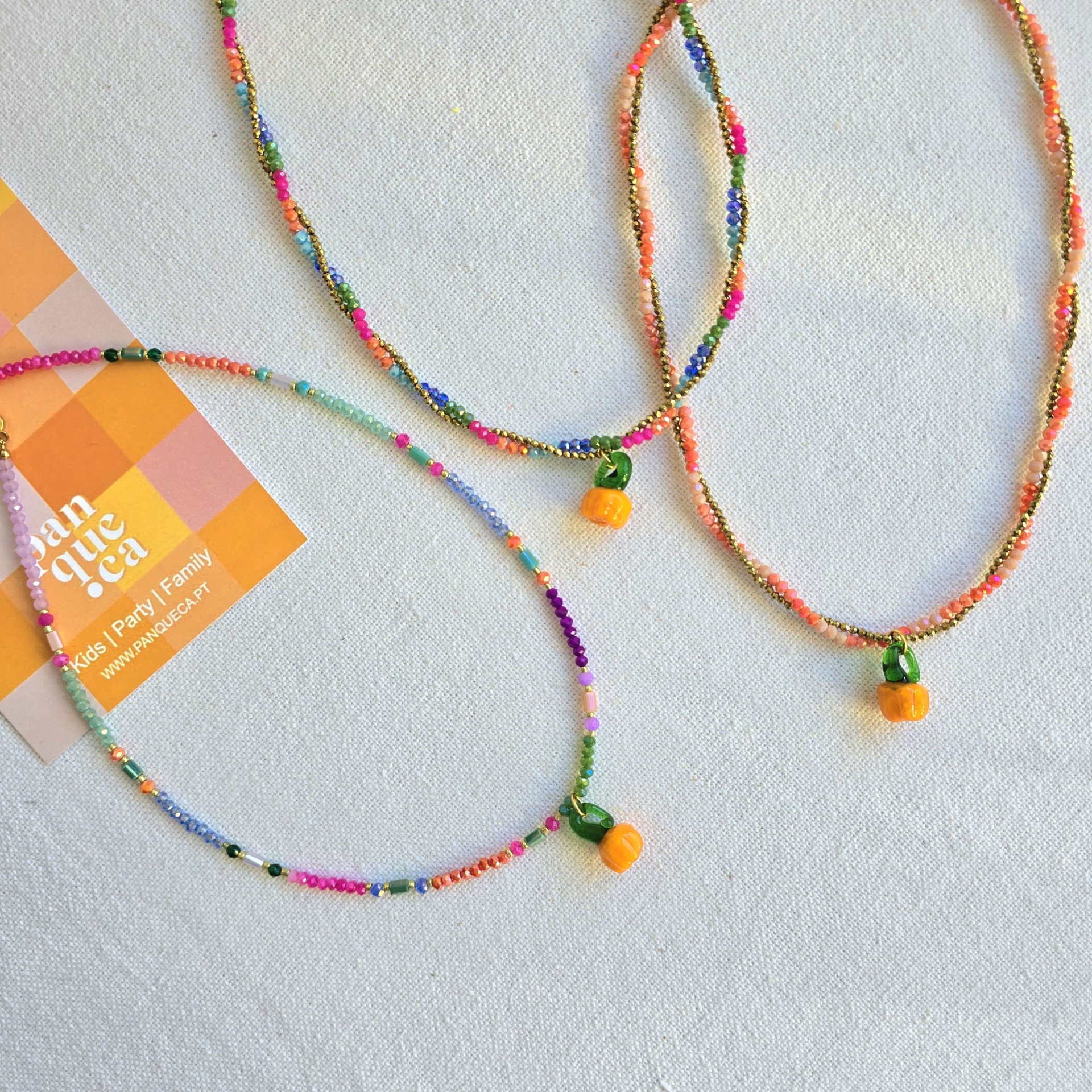Três colares de contas coloridas com pendentes de fruta laranja em fundo branco