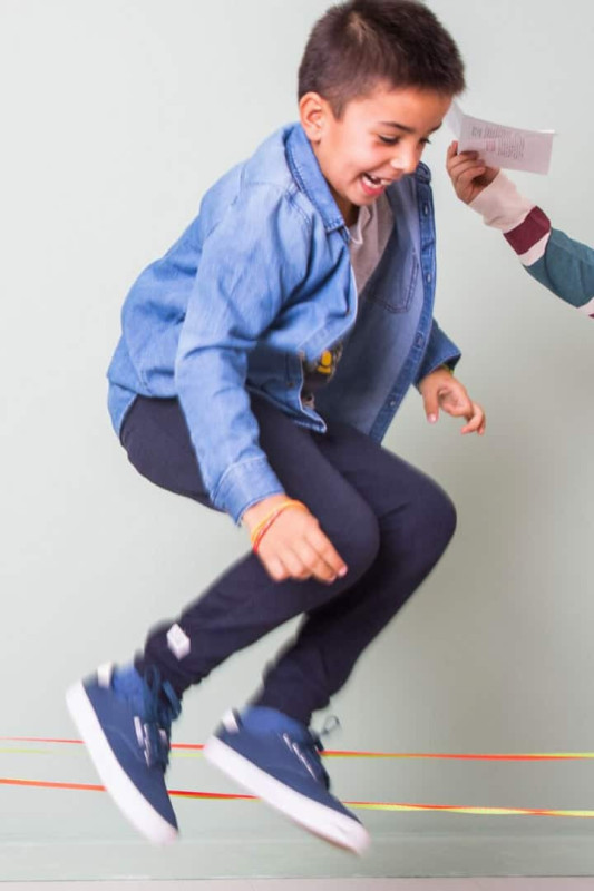 Criança a pular usando ténis azuis e calças pretas num ambiente interior