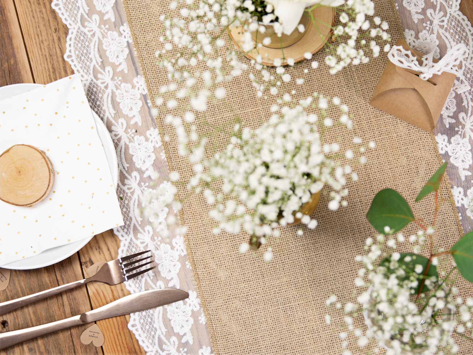 Mesa posta com caminho de mesa de juta e renda, pratos e talheres, flores brancas e envelope castanho