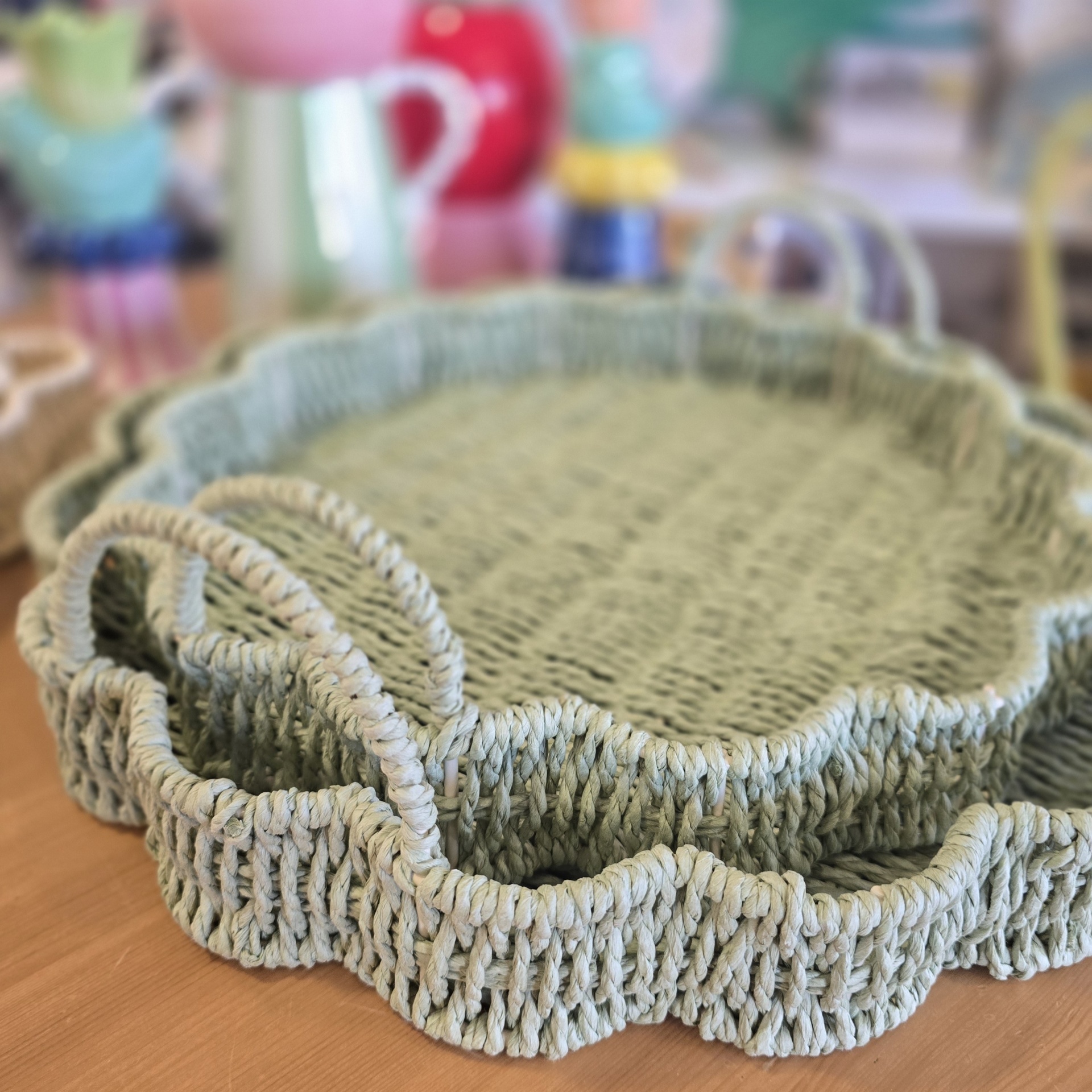 Tabuleiro oval verde claro em palha com bordas onduladas e alças sobre mesa de madeira