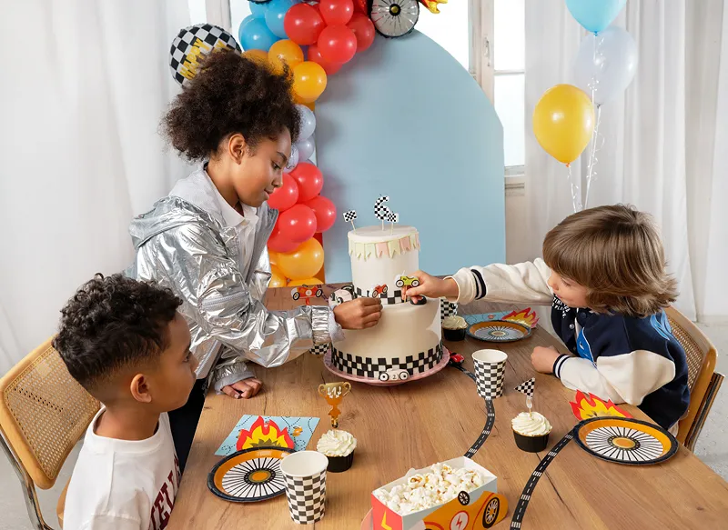 Festa infantil com bolo branco decorado em padrão xadrez preto e branco e crianças à volta da mesa