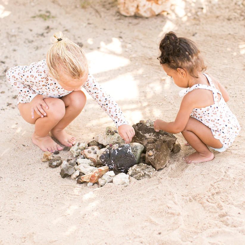 Duas crianças descalças brincam com areia e conchas