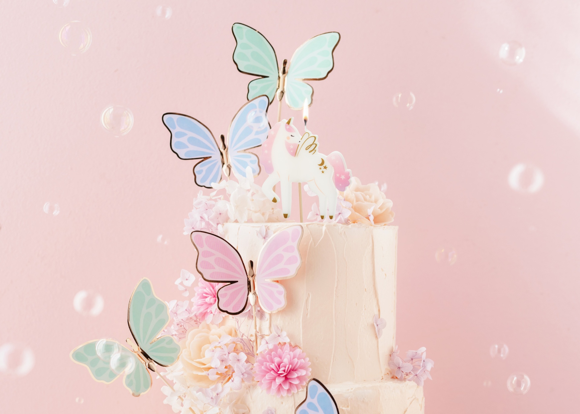 Bolo decorado com flores e borboletas coloridas e vela de unicórnio com crina rosa