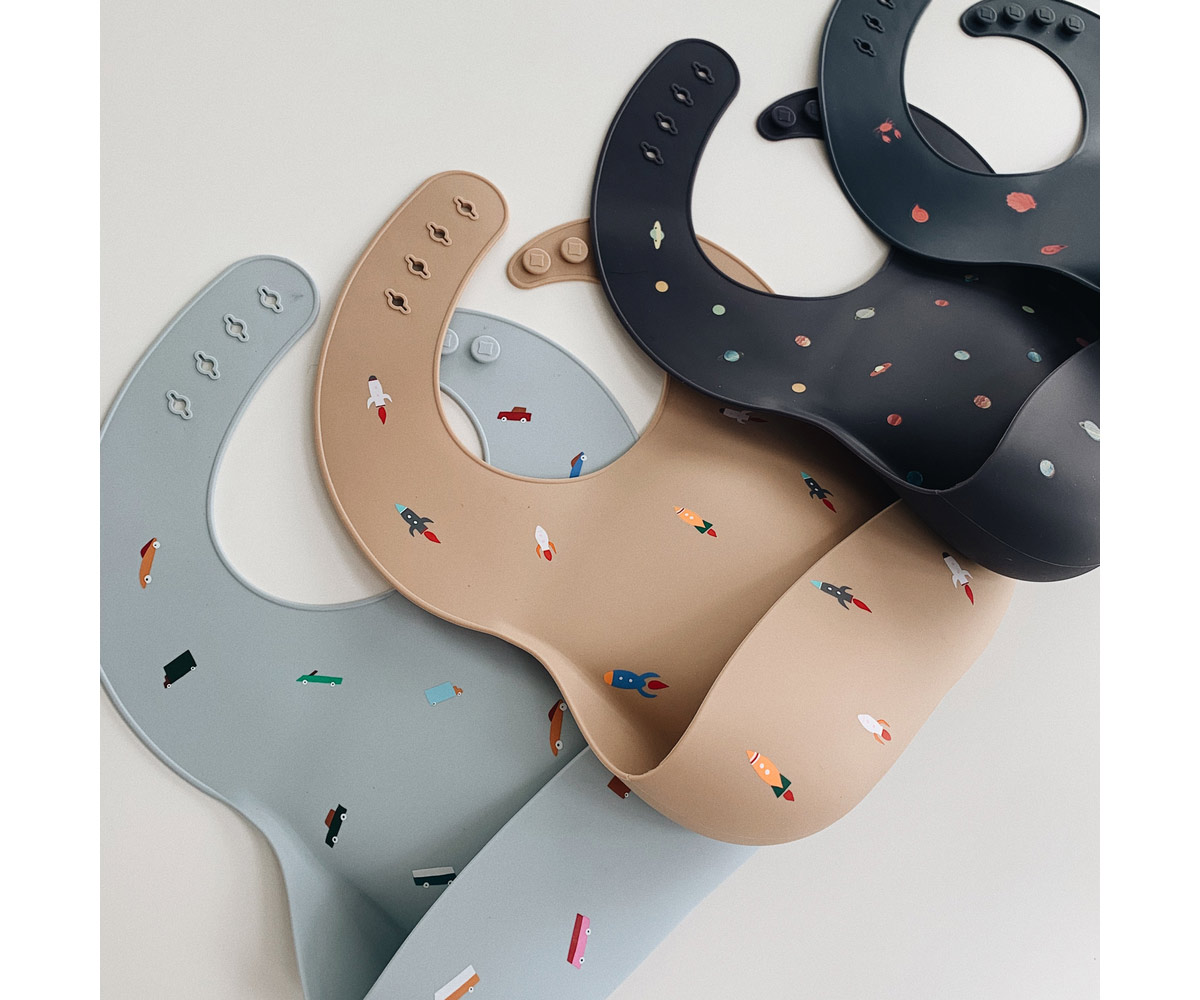 Três babetes de silicone com padrões coloridos em cinza, bege e preto.