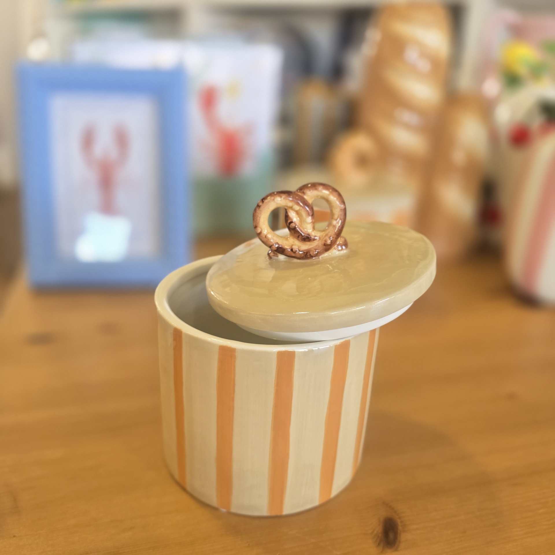 Pote em cerâmica com riscas verticais e tampa com pega em forma de pretzel.