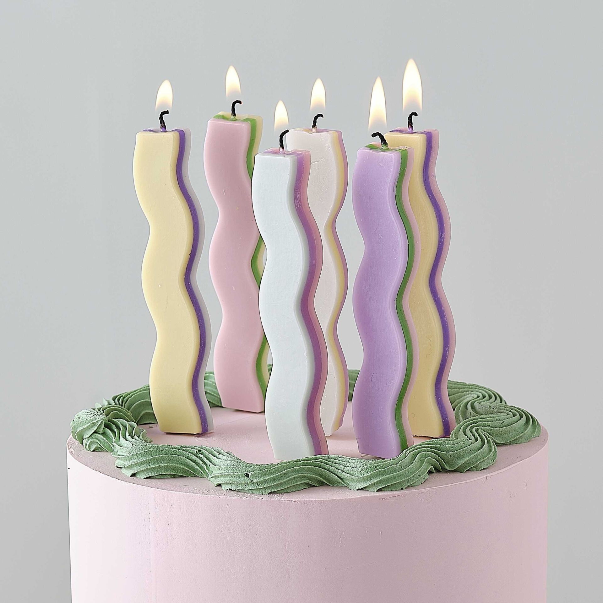 Bolo rosa claro com velas onduladas acesas em tons pastel
