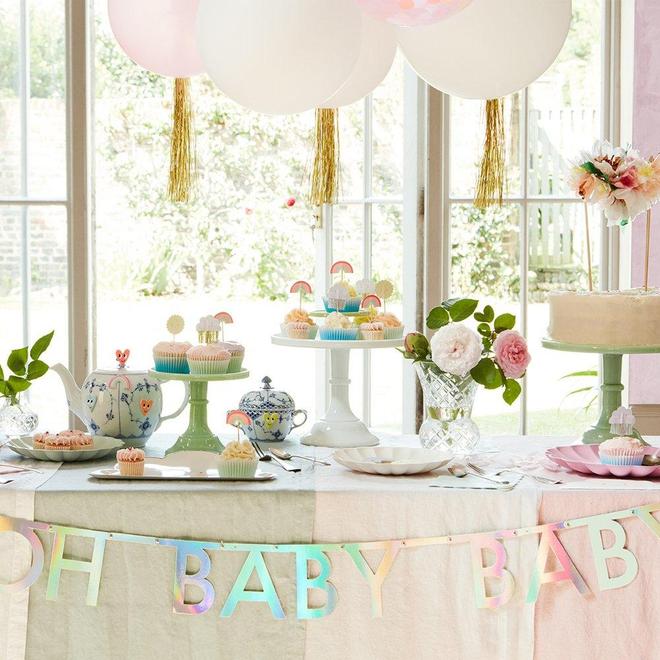 Mesa decorada para festa com cupcakes, bules, flores e balões com faixa 'OH BABY BABY'.