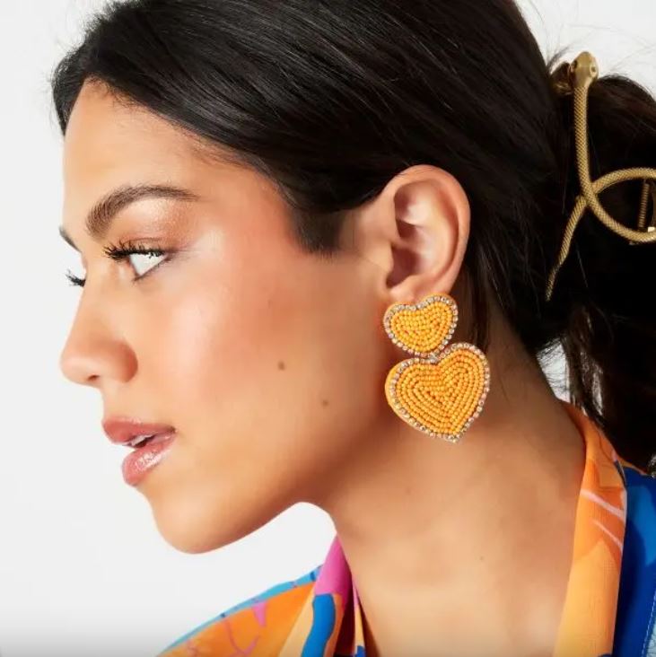 Brincos em forma de coração amarelos com detalhes lilás em mulher com roupa colorida