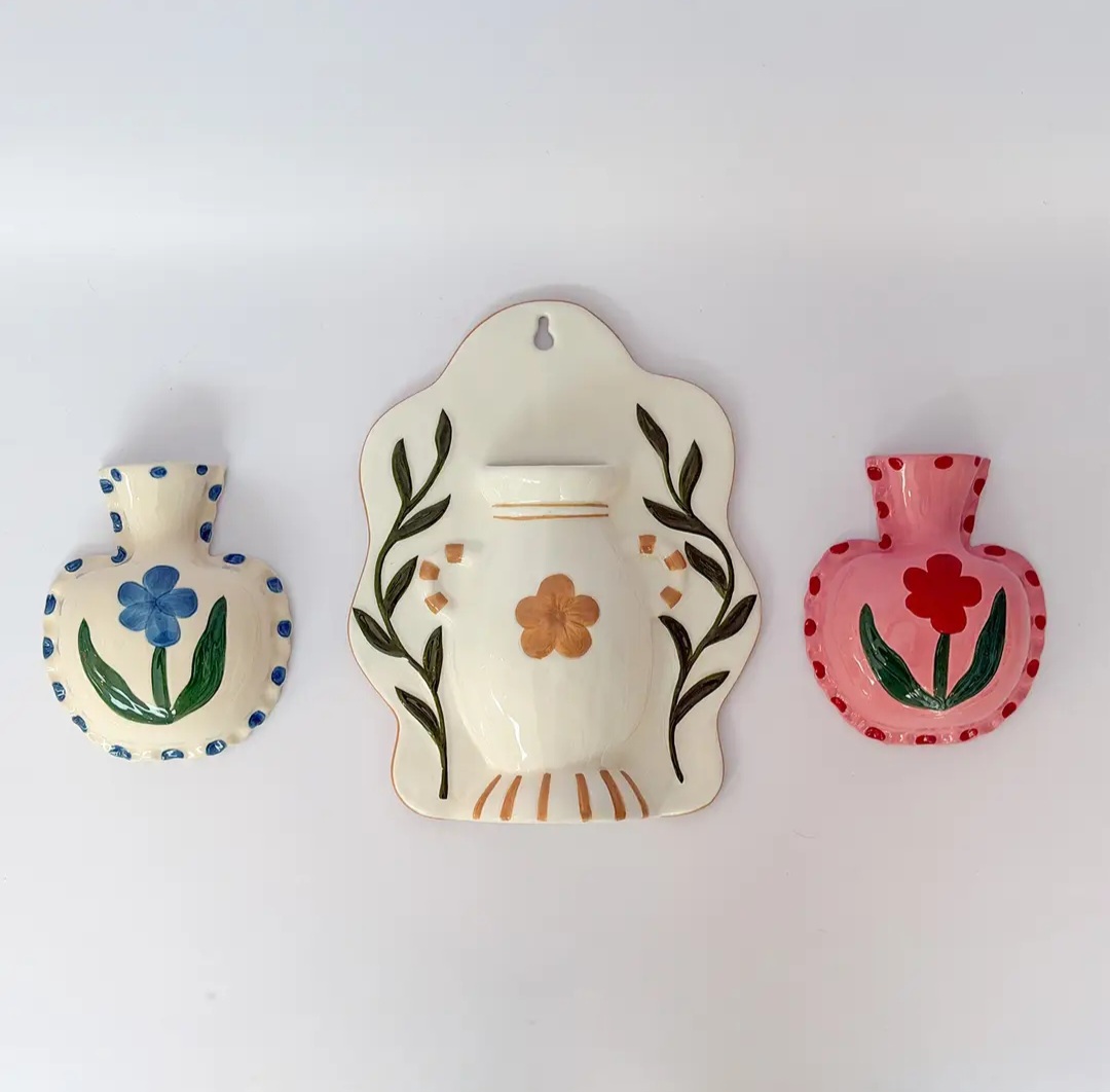 Três vasos de cerâmica decorativa em relevo com flores coloridas na parede