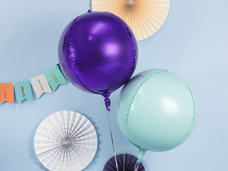 Balões redondos metálicos roxo e azul claro com decoração de papel ao fundo