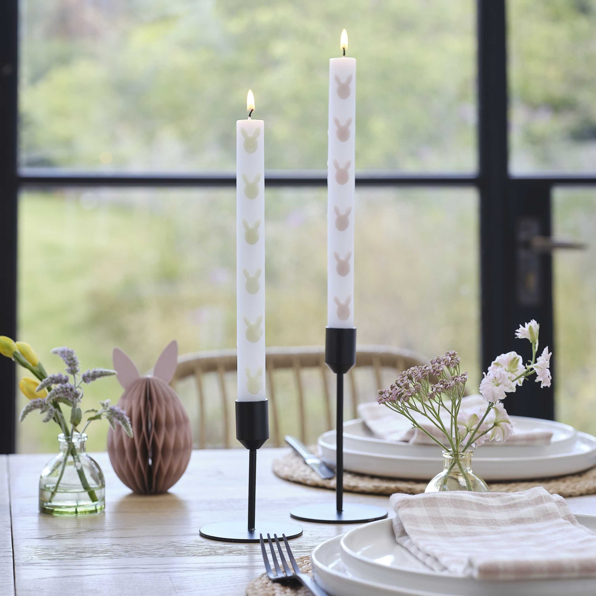 Mesa com castiçais pretos, velas brancas com coelhos e decoração de Páscoa