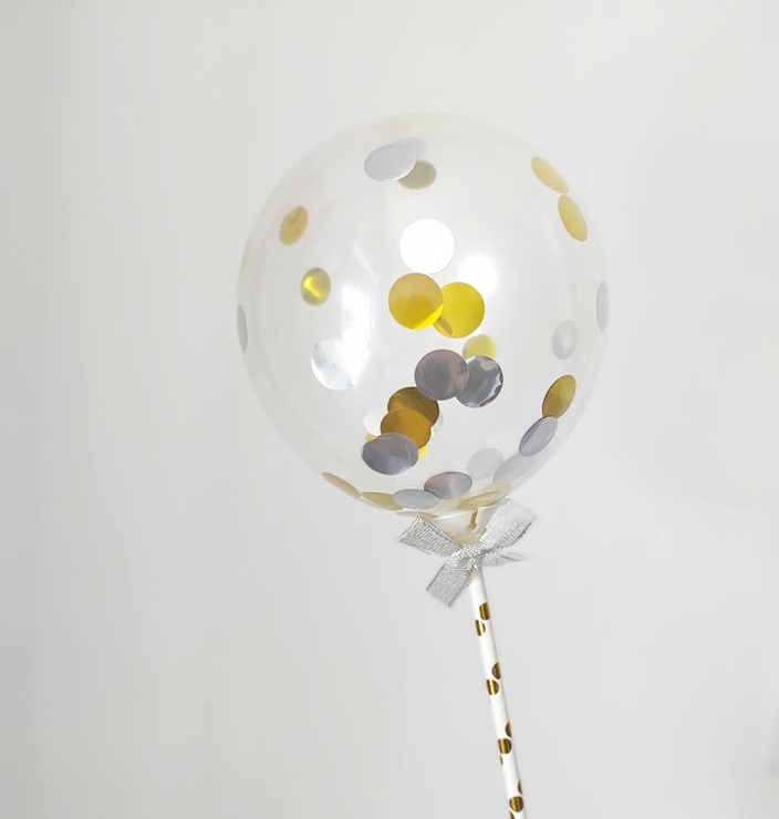 Balão transparente com confetes dourados e prateados e pau com laço