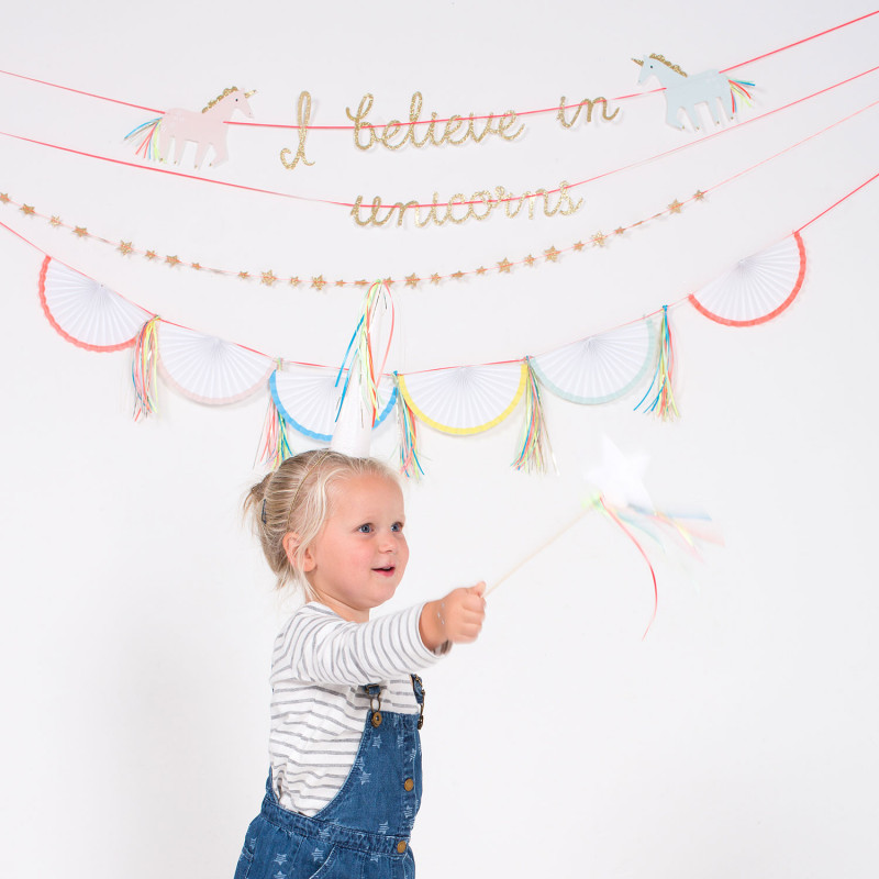 Criança com varinha mágica e decoração de unicórnios na parede