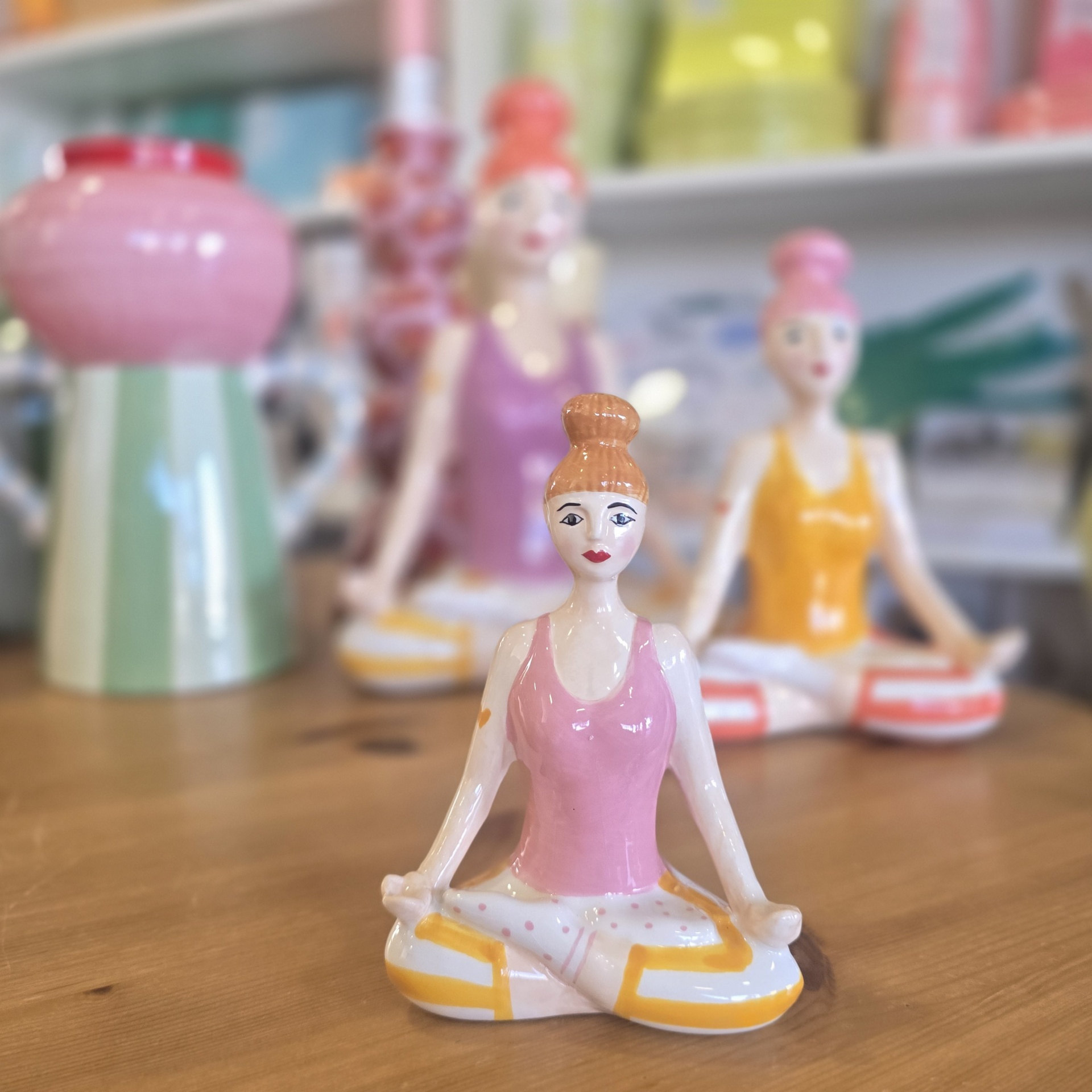 Figuras decorativas de mulher em cerâmica sentadas em posição de meditação com roupa rosa e amarela.