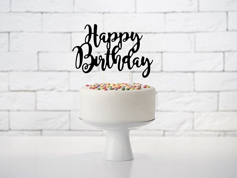 Bolo branco decorado com confeitos coloridos e topo com placa 'Happy Birthday'