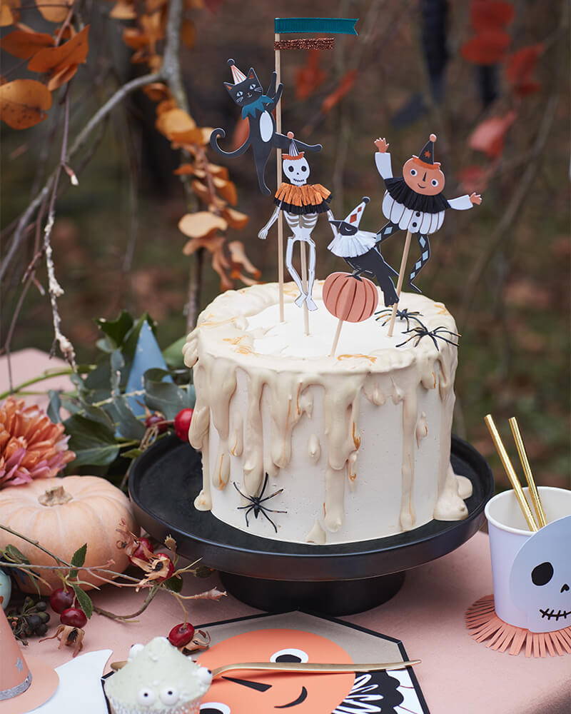 Bolo branco com decoração de Halloween e toppers temáticos numa mesa decorada