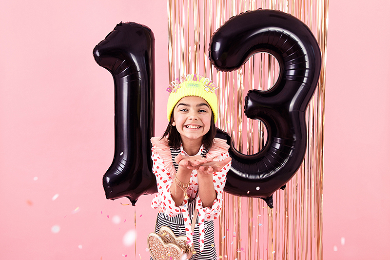 Menina com balões numéricos 1 e 3 em fundo rosa