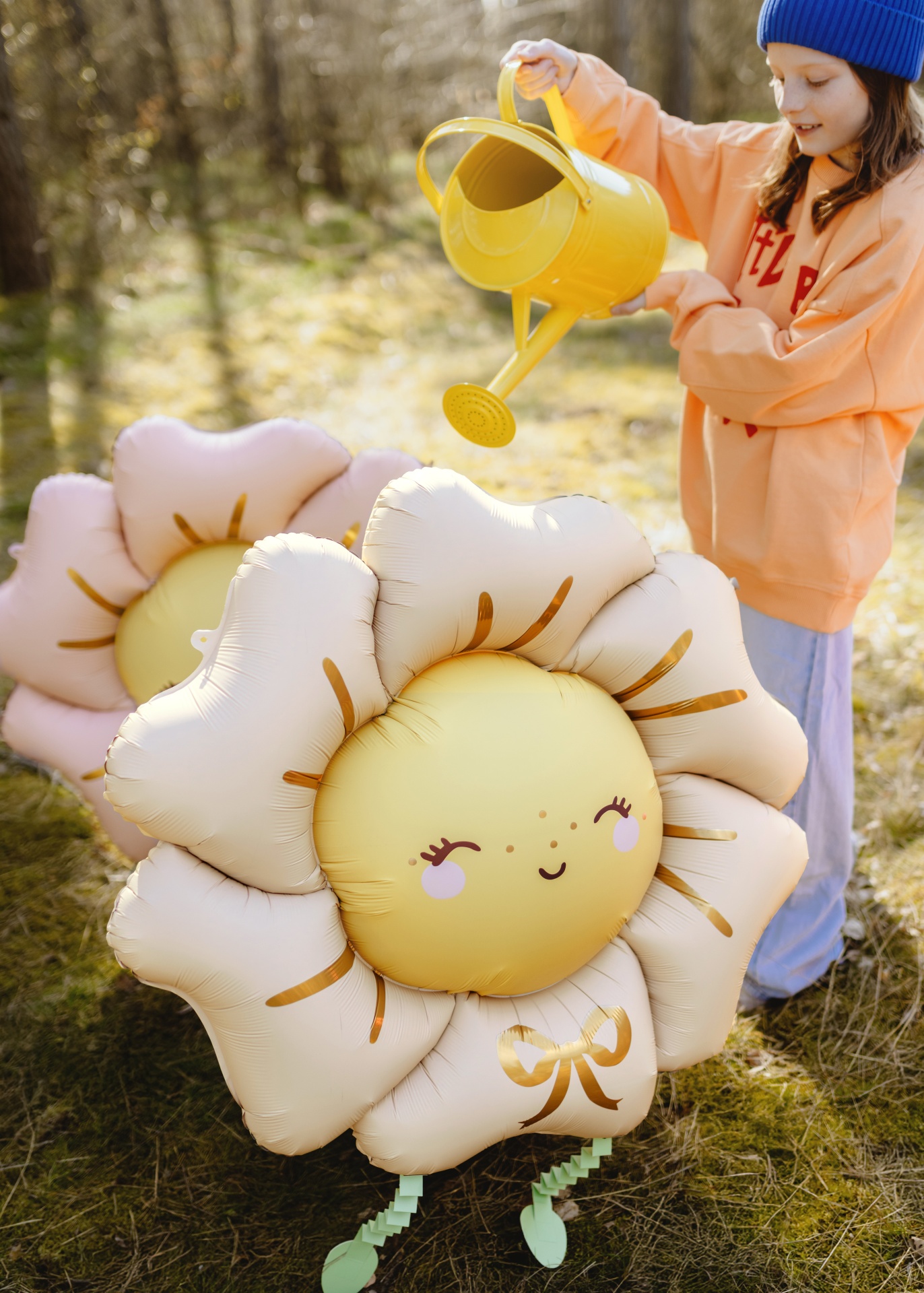 Balão em forma de flor sorridente com menina a usar regador amarelo ao ar livre