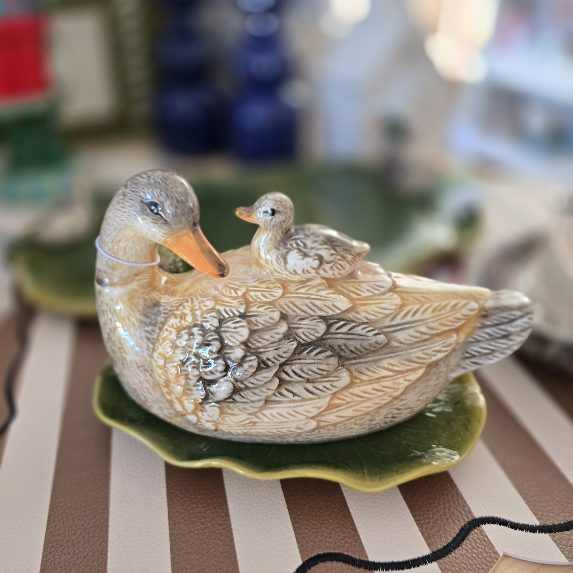 Escultura cerâmica de pato com patinho sobre o dorso em prato verde formato de folha