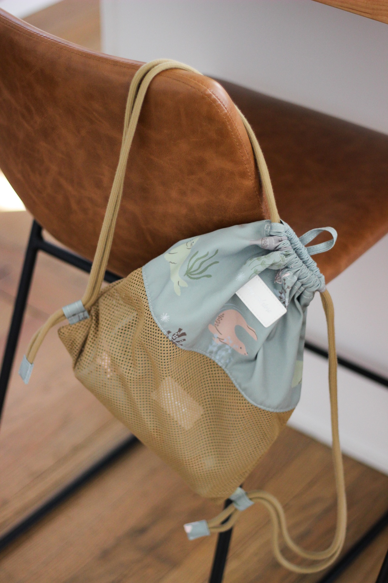 Mochila saco bege e azul claro com padrão de animais marinhos pendurada numa cadeira