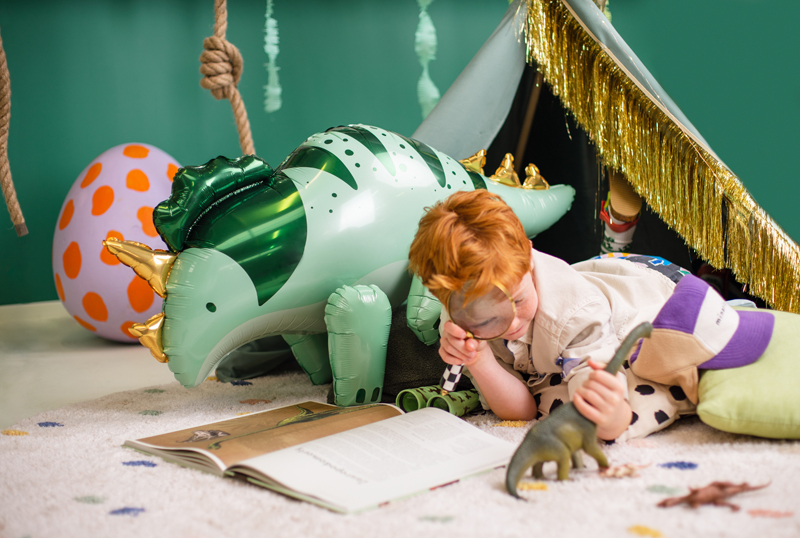 Criança de cabelo ruivo a brincar com brinquedos de dinossauros e dinossauro insuflável verde metálico