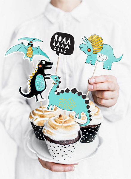 Cupcakes decorados com figuras de dinossauros azul, amarelo e preto em canecas de papel com padrão de bolinhas pretas.