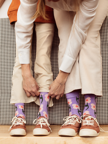 Pessoas com meias florais roxas, calças beges e sapatos castanhos sentadas num sofá pied-de-poule