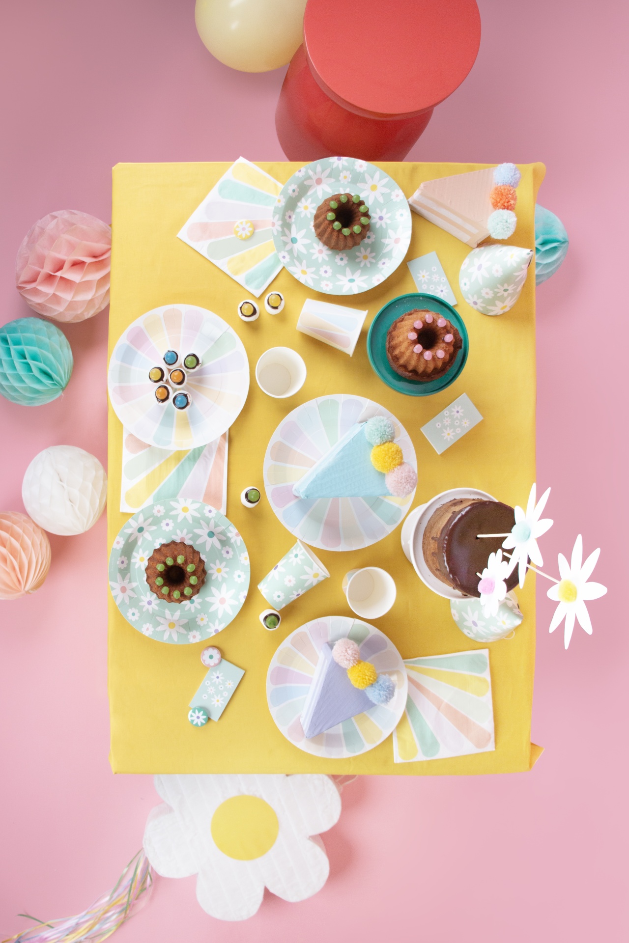 Mesa de festa decorada com pratos, copos, chapéus, bolo e balões coloridos