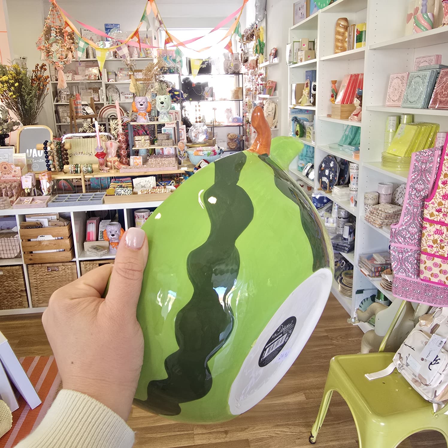 Vaso cerâmico verde com padrão ondulado preto segurado por uma mão em loja colorida