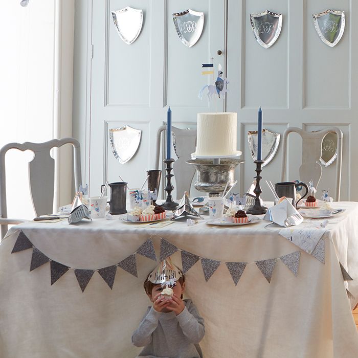 Mesa de jantar decorada com toalha branca, guirlanda de tecidos e velas, criança sentada em frente.