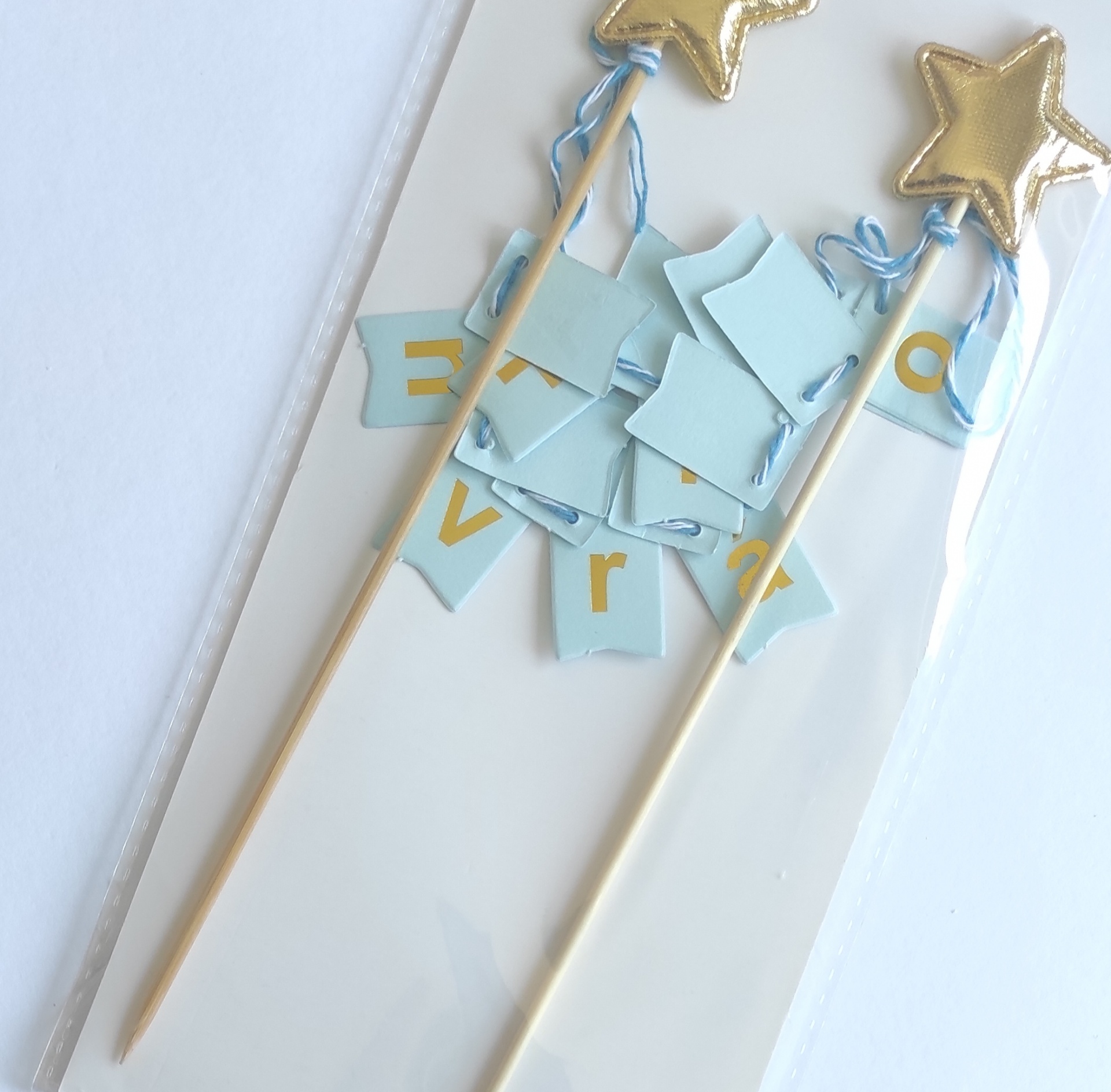 Espetos de madeira com estrelas douradas e pedaços de papel azul com letras douradas