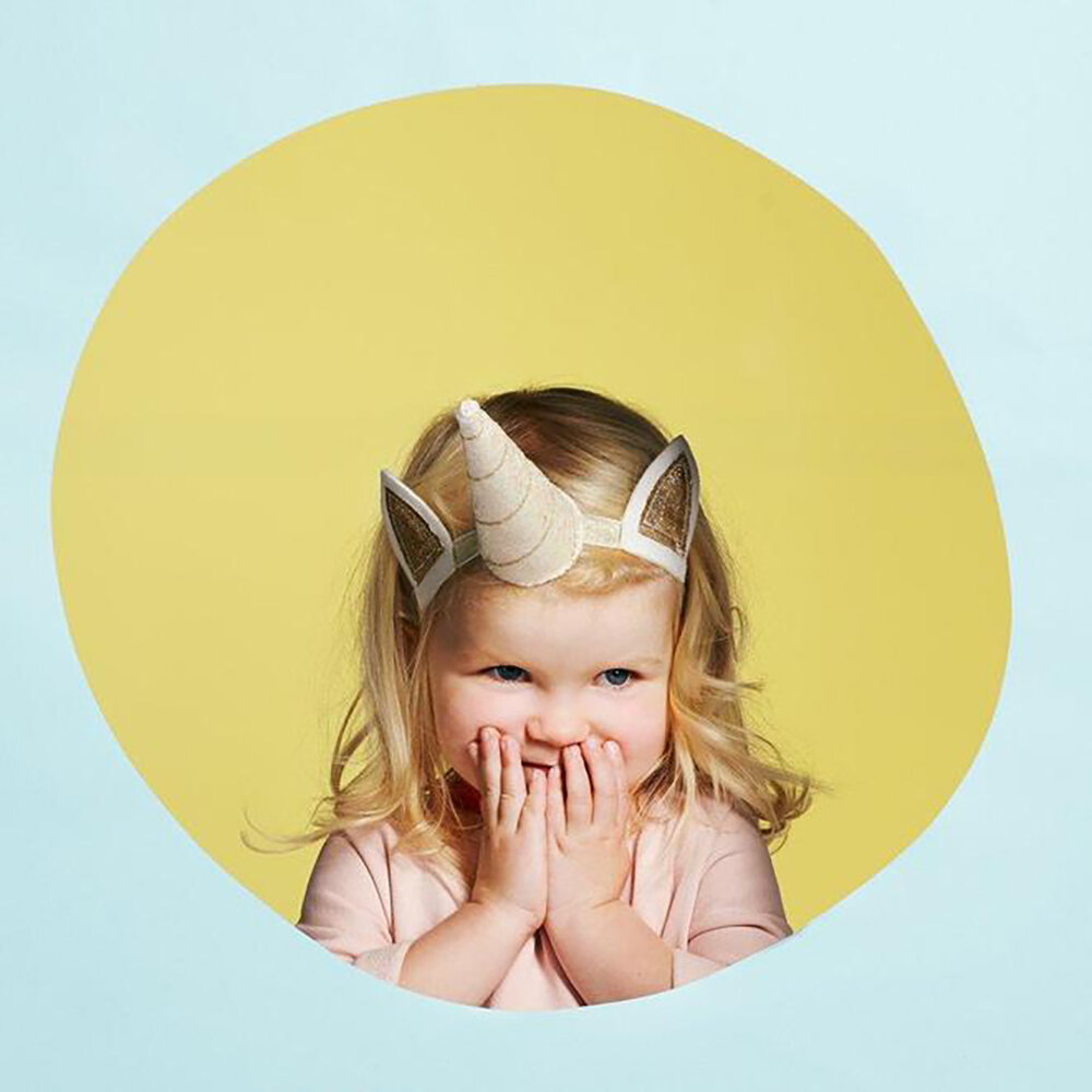 Criança com tiara de unicórnio num círculo amarelo num fundo azul