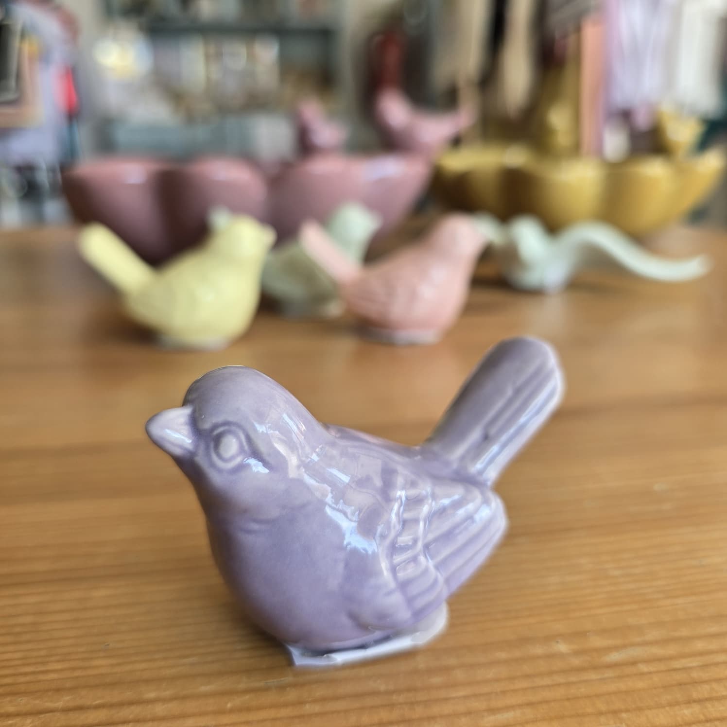 Pássaros decorativos em cerâmica colorida em tons pastel sobre mesa de madeira