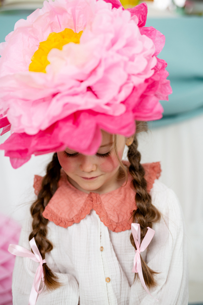 Criança com vestido branco e chapéu de flor rosa grande