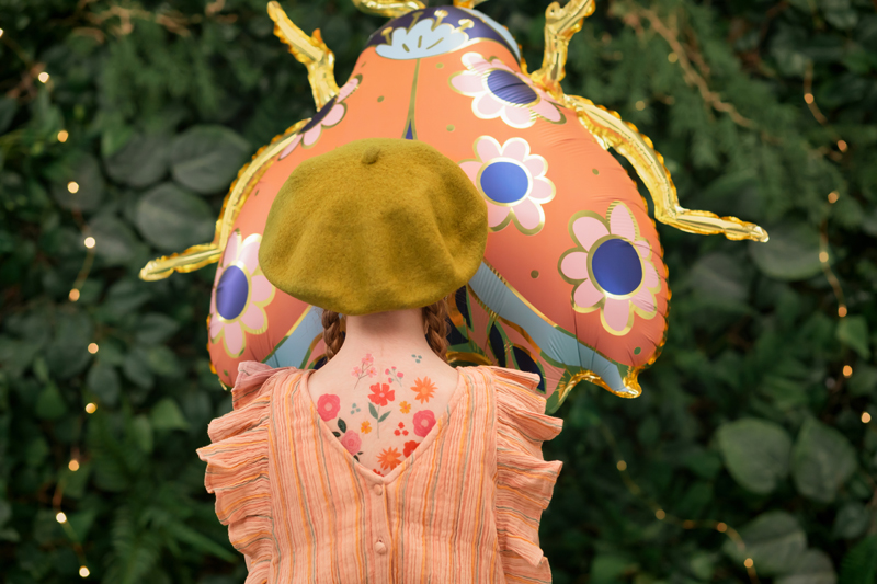 Criança com vestido cor de pêssego e boina verde segurando balão de borboleta floral ao ar livre