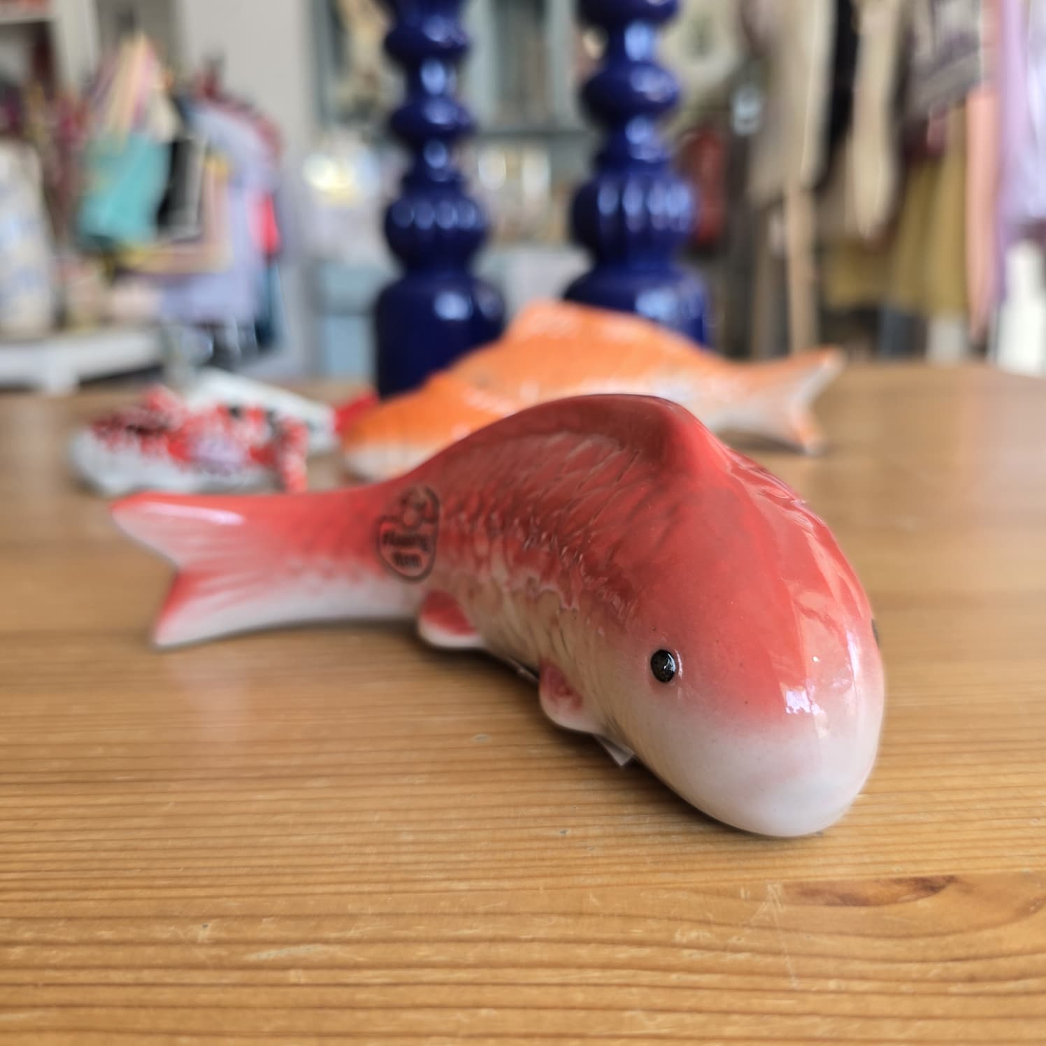 Peixe decorativo cerâmico vermelho e branco com texto FISHERMAN MARU num ambiente interior.