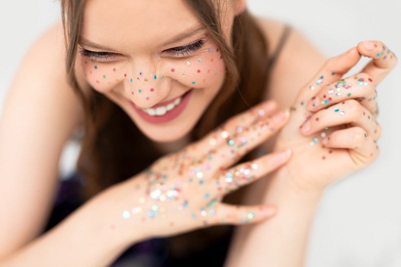Mulher sorridente com brilhos coloridos no rosto e mãos