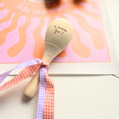 Colher de pau com fitas e texto a maria fan 2 sobre tecido rosa e laranja