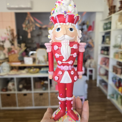 Figura Quebra-Nozes em madeira vermelha, branca e rosa com confetis, segurada numa mão em loja.