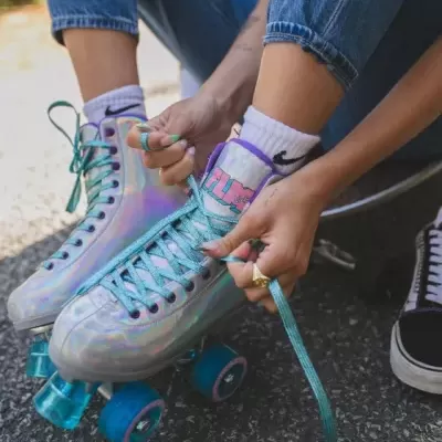 Patins de rodas prateados iridescentes com atacadores azuis e rodas azul-turquesa em pessoa sentada a atar os atacadores.