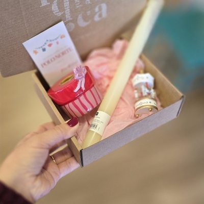 Caixa de cartão com vela, frasco vermelho, papel de seda rosa e mini-rolha branca com etiqueta.