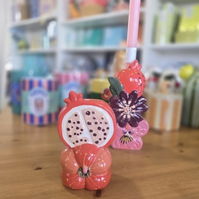 Dois objetos decorativos de cerâmica em forma de romã e flores com vela rosa