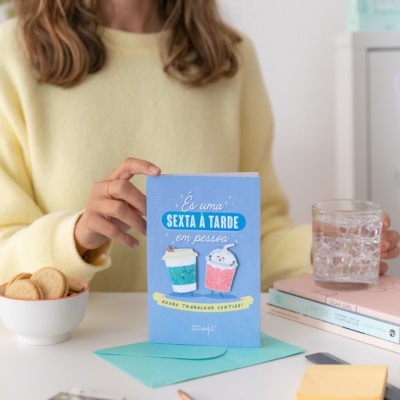 Cartão azul com ilustração de dois cafés e texto, sobre mesa com vários objetos