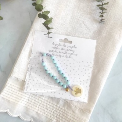 Pulseira colorida para criança com pingente numa embalagem branca sobre pano bege.